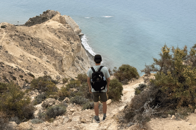 Túrázó a Cape Aspro túraútvonal meredek, sziklás ösvényén Pissouri közelében, háttérben a fehér sziklafalak és a tenger Cipruson